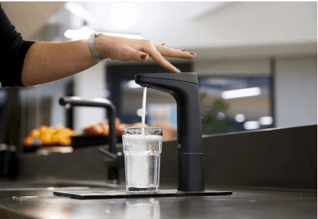 Improve Water Quality in your New Apartment 1 A hand holding a glass under a black water dispenser in a new apartment, as water of impeccable quality flows into the glass.