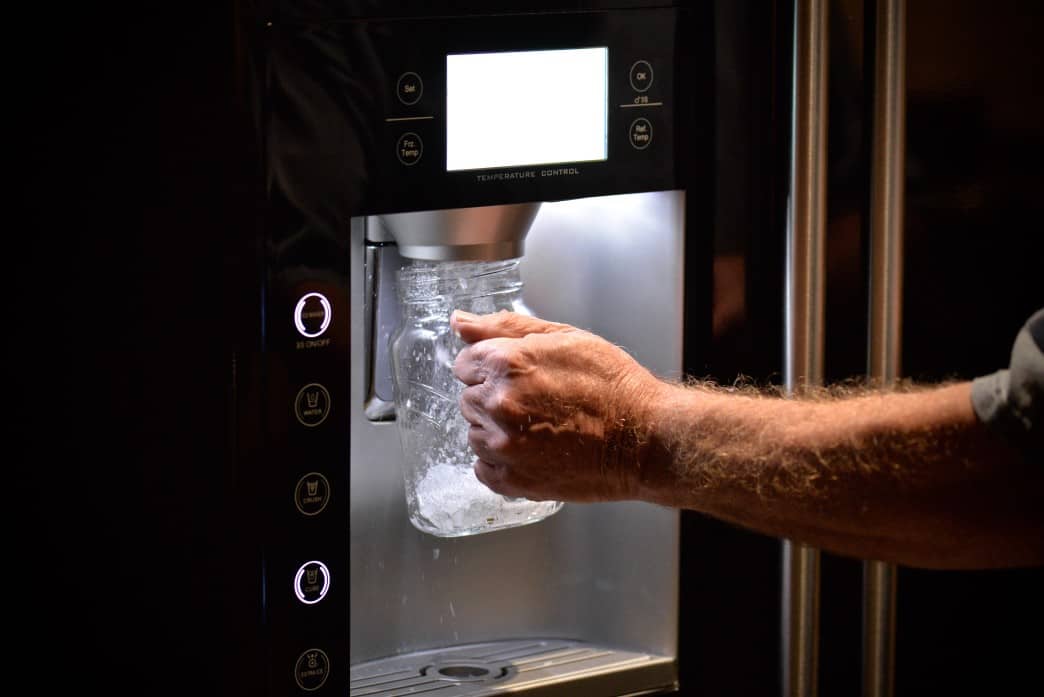 Improve Water Quality in your New Apartment 3 A person in their new apartment holds a glass jar under an automatic ice dispenser built into the refrigerator door, ready to enjoy refreshing, high-quality water.