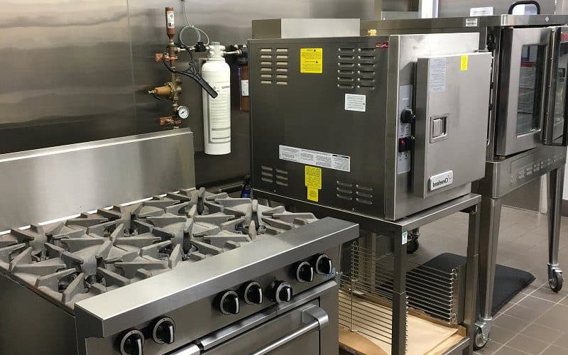 Gas Plumbing 2 New commercial kitchen setup with a stainless steel stove, an oven, and a water filter installation on the wall.