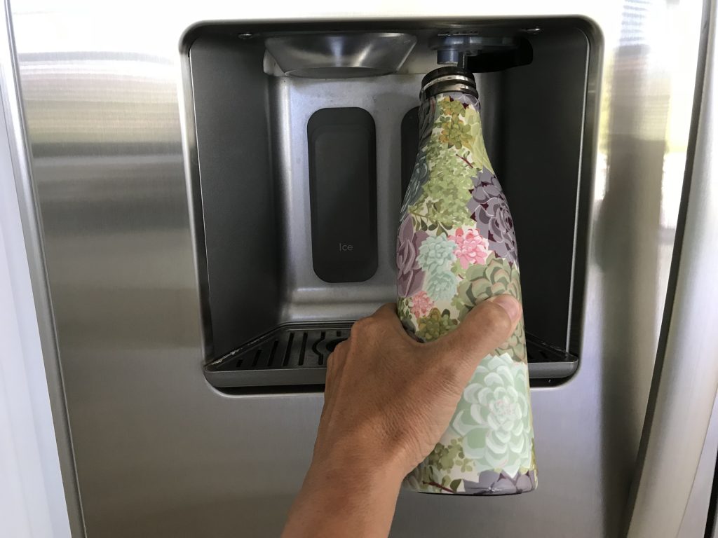 Water supply to fridge 1 A hand fills a floral-patterned water bottle from the water supply to the fridge's dispenser.
