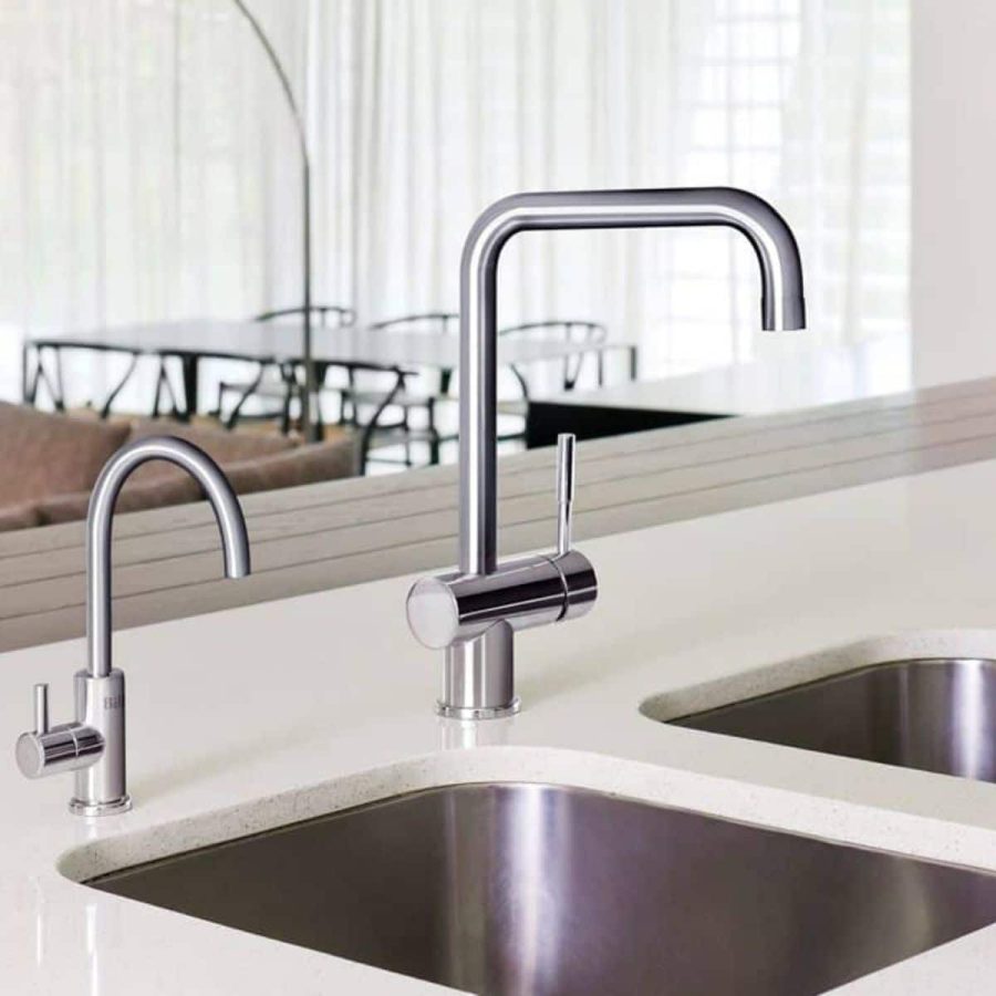 A modern kitchen with a double basin sink and two sleek, stainless steel faucets reflects expert plumbing services. The background shows a dining area with a table and chairs. A modern kitchen with a double basin sink and two sleek, stainless steel faucets reflects expert plumbing services. The background shows a dining area with a table and chairs.