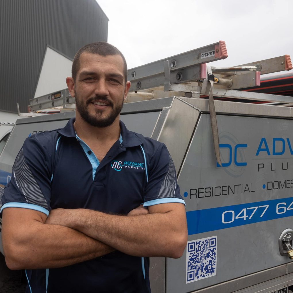 A man stands with arms crossed in front of a utility vehicle adorned with the branding “DC Advance Plumbing.” The vehicle, essential for providing top-notch plumbing services, is equipped with ladders and pipe materials. A man stands with arms crossed in front of a utility vehicle adorned with the branding "DC Advance Plumbing." The vehicle, essential for providing top-notch plumbing services, is equipped with ladders and pipe materials.