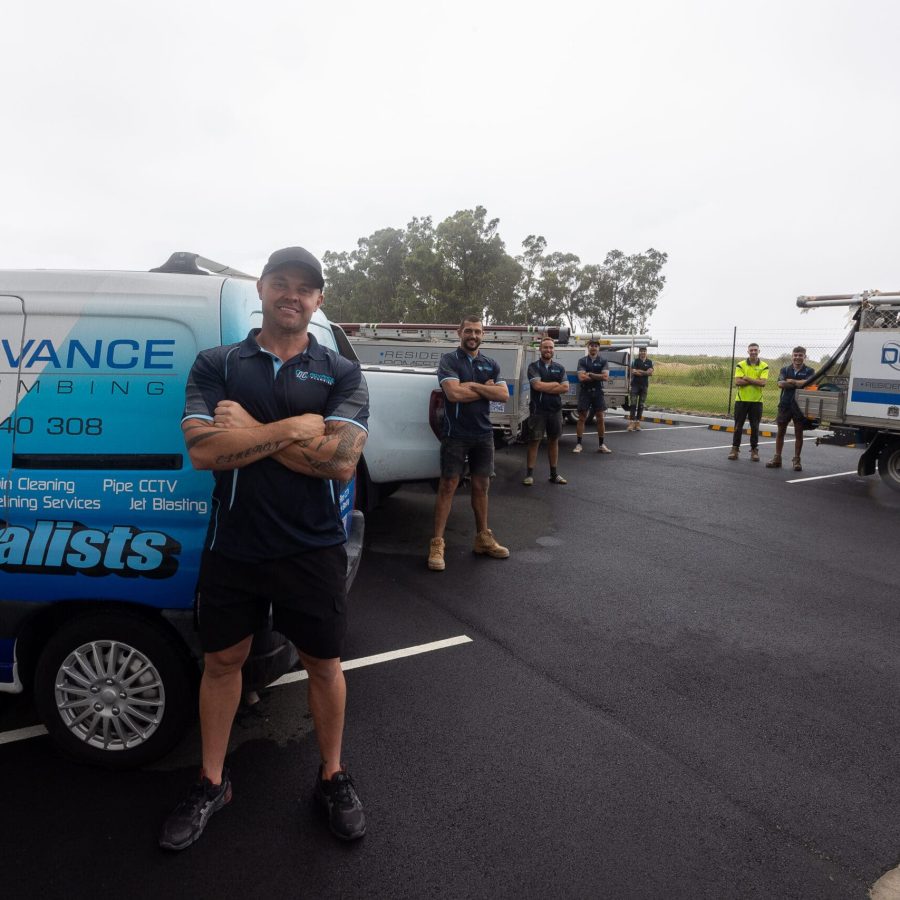 Six men in work uniforms stand next to two company vans labeled “Advance Plumbing” in a parking lot. One man, arms crossed, symbolizes confidence in their plumbing services, while the others stand behind the vehicles. Six men in work uniforms stand next to two company vans labeled "Advance Plumbing" in a parking lot. One man, arms crossed, symbolizes confidence in their plumbing services, while the others stand behind the vehicles.